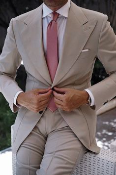 a man in a tan suit and pink tie is sitting on a white bench with his hands behind his back