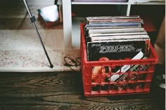 a red plastic container filled with records on top of a wooden floor