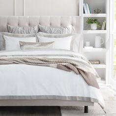 a bed with white sheets and pillows in a bedroom next to a bookshelf