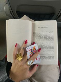 a woman is holding an open book and two playing cards in her hand while sitting down