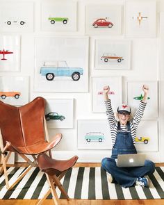 a woman sitting on the floor with her laptop in front of a wall full of cars