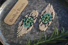 two beaded owl earrings sitting on top of a metal plate next to a plant