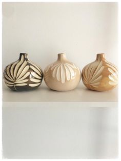 three vases sitting on top of a white shelf