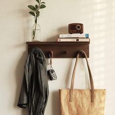 a purse and coat hang on a wall next to a book shelf with a camera