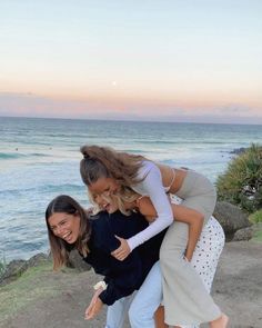 three women standing on the edge of a cliff by the ocean with their arms around each other