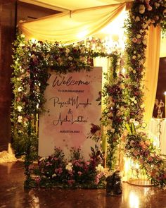 a welcome sign is surrounded by flowers and greenery on the floor at a wedding