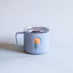 a white and blue coffee cup with a tree on the side sitting on a table