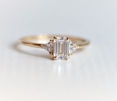 a three stone diamond ring on a white surface with the center setting in yellow gold