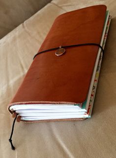 an open brown leather book on top of a white bed with a string around it