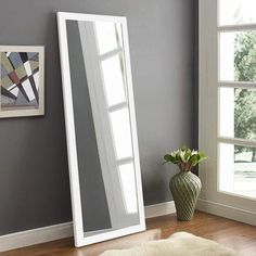 a white floor mirror sitting on top of a hard wood floor next to a window