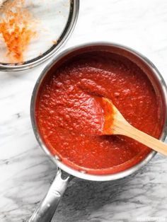 a wooden spoon in a saucepan filled with tomato sauce on a marble counter top