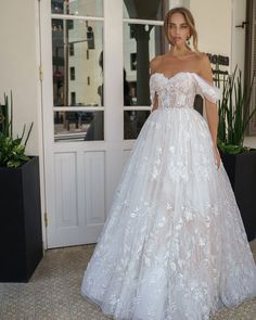 a woman in a white wedding dress standing on the sidewalk with potted plants behind her