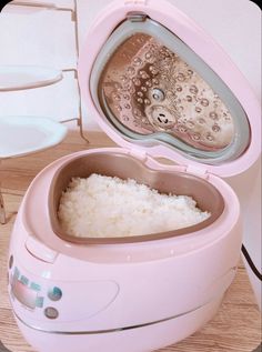 a pink lunch box with rice inside on a wooden table next to a white chair