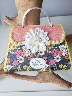 a handbag made out of fabric with flowers and pearls on the handle is sitting on a tree branch