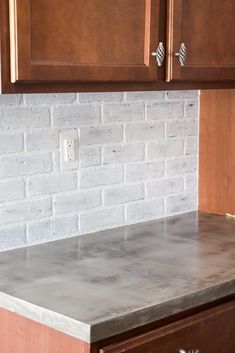 a kitchen counter top with wooden cabinets and white brick wall in the backround