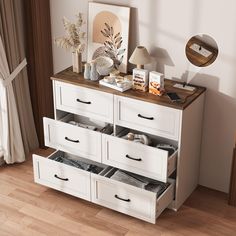 a white dresser with drawers and pictures on the top shelf in front of a window