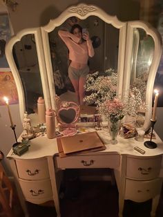 a woman taking a selfie in front of a dressing table with flowers and candles