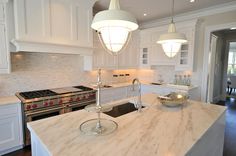 a white kitchen with marble counter tops and an island in front of the stove top