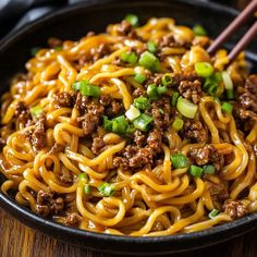 a black bowl filled with noodles and ground beef on top of a wooden table next to chopsticks