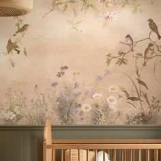 a baby crib next to a wall with flowers and birds painted on it