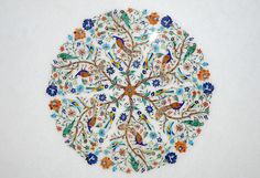 an intricately decorated plate with birds and flowers on it's side, sitting on a white surface