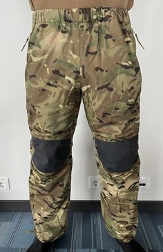 a man in camouflage pants and boots is standing on the floor with his hands behind his back