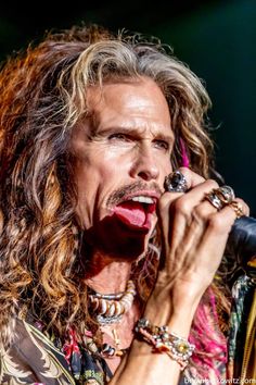 a man with long hair holding a microphone in his hand and singing into the microphone