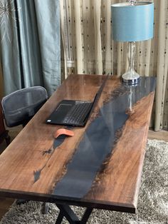 a laptop computer sitting on top of a wooden table in front of a blue lamp