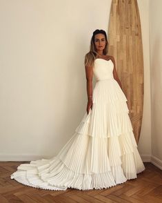 a woman standing in front of a surfboard wearing a white dress with tiered layers