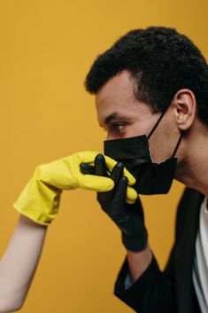 a man in a black suit and yellow gloves is covering his face with a mask