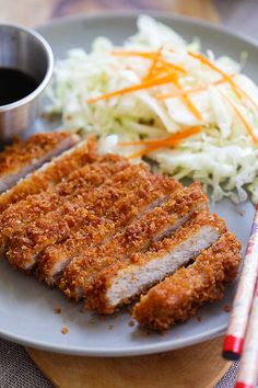 a plate with meat, coleslaw and chopsticks next to it on a table