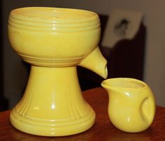 a yellow vase sitting on top of a wooden table next to a small white cup