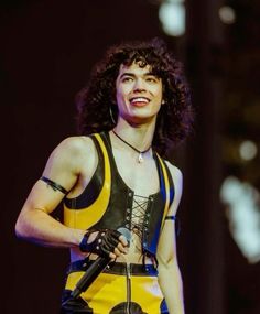 a woman with curly hair is wearing a yellow and black outfit while holding a microphone