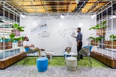 two men are in an office setting with plants on the walls and chairs around them