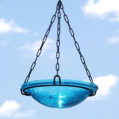 a blue glass bowl hanging from a chain on a clear day with clouds in the background