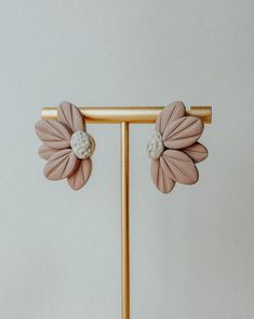 two pink flower shaped earrings with pearls on them sitting on a gold stand against a white wall