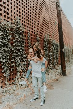 a man carrying a woman on his back in front of a brick wall with vines