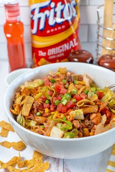 a white bowl filled with taco salad next to tortilla chips and condiments