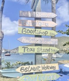 a wooden sign with many different signs attached to it's sides in front of the ocean