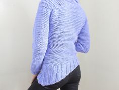 a woman wearing a blue sweater and black pants is looking at the back of her jacket