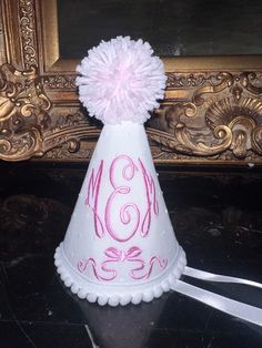 a white party hat with pink writing and a pom - pom on top