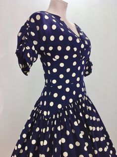 1950's Navy Blue & Creamy White Polka-Dot Drop-Waist Dress. Quality cotton fabric with a fitted bodice and a drop waist, a full gathered skirt, and a neckline that V'S in the front as well as the back. The drop waist is 3 inches lower on the sides than in the front.. which adds interest and wow factor to the silhouette. Such a beautiful dress!! There is a metal zipper that runs down the back of this dress for that perfect tailored hourglass fit. This garment is in EXCELLENT VINTAGE CONDITION Fitted Rockabilly Dresses For Vintage Fashion, Fitted Short Sleeve Rockabilly Vintage Dress, Vintage Polka Dot Lined Dresses, Fitted Retro Polka Dot Vintage Dress, Retro Fitted Polka Dot Vintage Dress, Fitted Polka Dot Vintage Dress, 1970s Style Fitted Vintage Dress For Vintage Events, Fitted 1950s V-neck Dress, Fitted 1950s Polka Dot Dresses