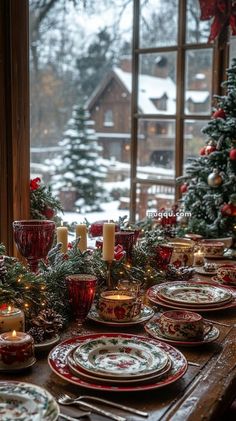 a table set for christmas with plates and candles on it in front of a window