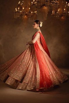 a woman in a red and gold wedding dress with a chandelier hanging from the ceiling