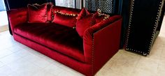 a red couch sitting in front of a window next to a black curtain and white tile floor