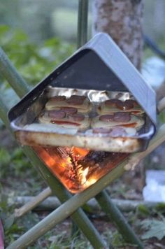 hotdogs cooking on an outdoor grill in the woods with flames coming from them