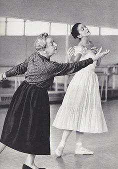 two women are dancing together in an old black and white photo, one is wearing a skirt