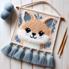 a crocheted fox with tassels and yarn next to it on a white wooden surface