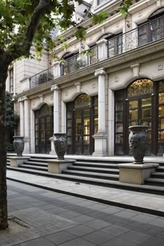 two large vases sitting on the side of a building next to a tree in front of it