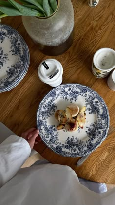 a person sitting at a wooden table with plates and cups on top of the table